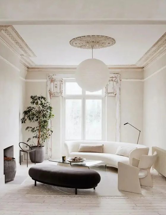 a refined neutral living room with a white curved sofa and a chair, a black curved ottoman, an acrylic coffee table and a potted plant