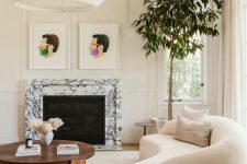 a refined neutral living room with molding, a white marble fireplace, a curved boucle sofa, a coffee table and some artwork