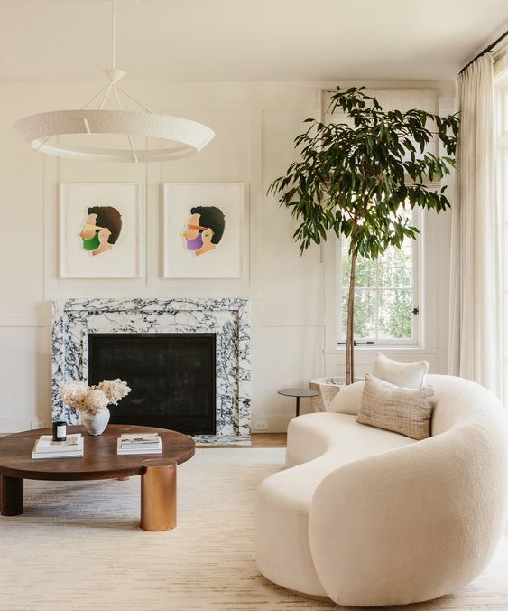 a refined neutral living room with molding, a white marble fireplace, a curved boucle sofa, a coffee table and some artwork