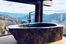 a rustic bathroom with a fantastic view, wooden floors and a dark stone bathtub carved of a single piece of stone