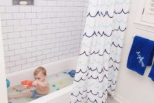 a sea-inspired kids’ bathroom with a shark rug, a catchy wave curtain, blue towels for a chic and stylish look