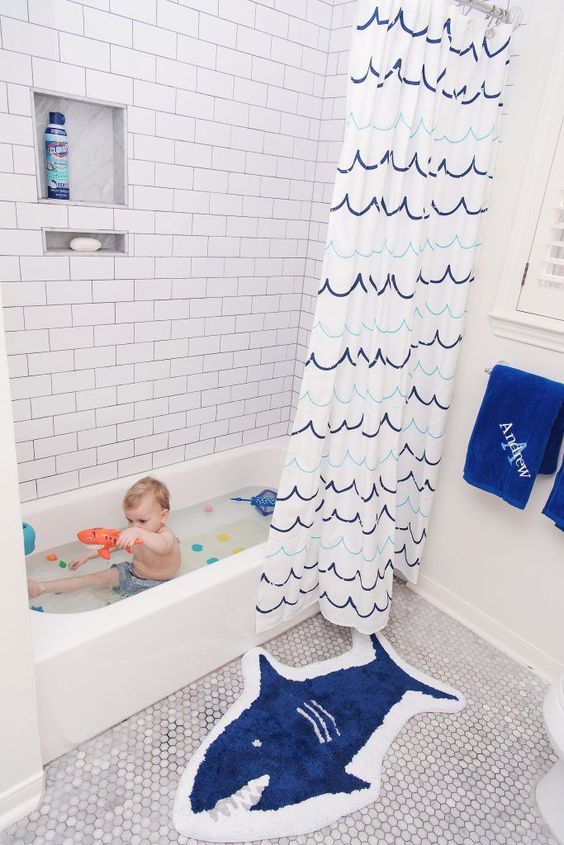 A sea inspired kids' bathroom with a shark rug, a catchy wave curtain, blue towels for a chic and stylish look