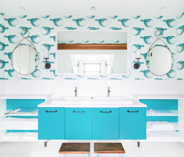 A sea inspired kids' bathroom with funny fish wallpaper, a bright blue vanity and open shelving