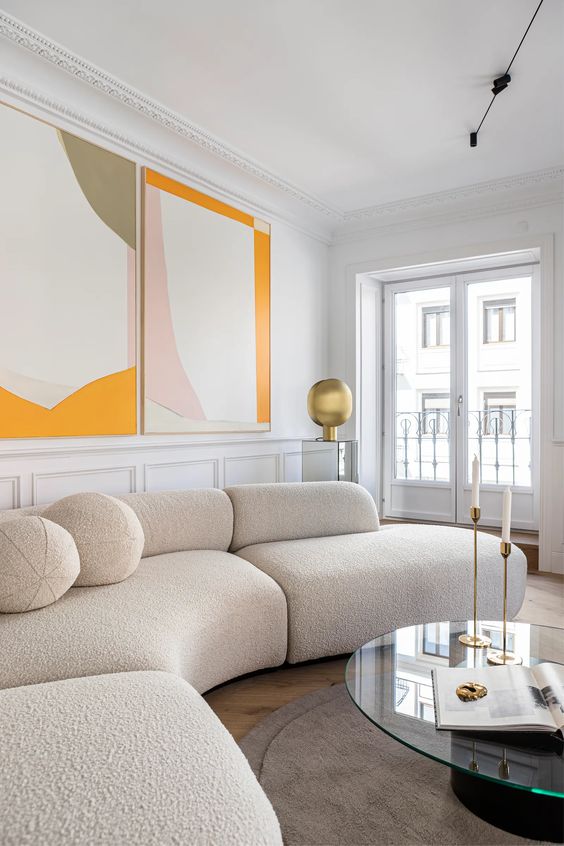 a serene living room with a creamy boucle curved sofa, a round coffee table, large abstract art and some brass decor