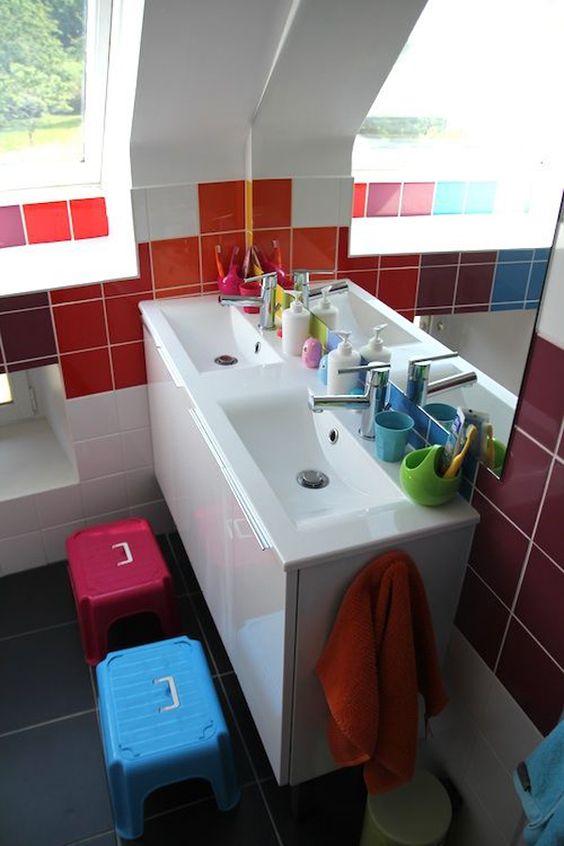 a small modern kids' bathroom with colorful tiles on the walls and bright stools plus bright accessories