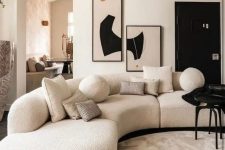a stylish and contrasting living room with a white boucle curved sofa, a black table and eye-catchy artwork on the wall