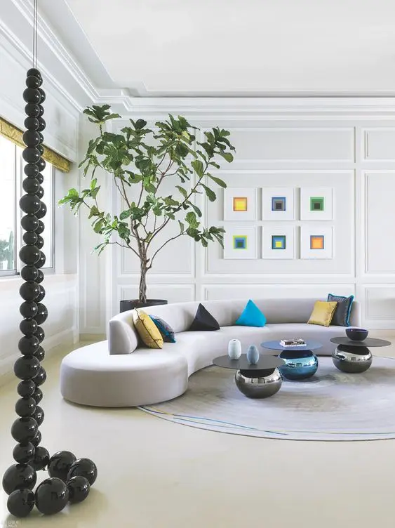 a stylish contemporary living room with molding, a grey curved sofa with colorful pillows, a gallery wall and coffee tables