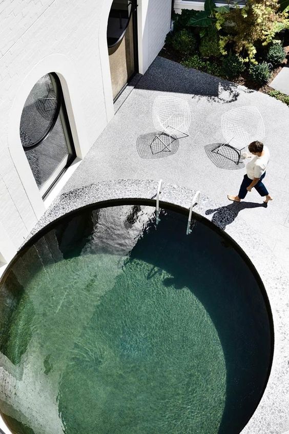 a super stylish minimalist backyard done with stone and concrete, with a round pool clad with stone