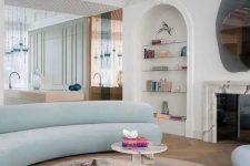 a whimsical living room with a white marble fireplace, built-in shelves, a light blue curved sofa, marble tables and cool rugs