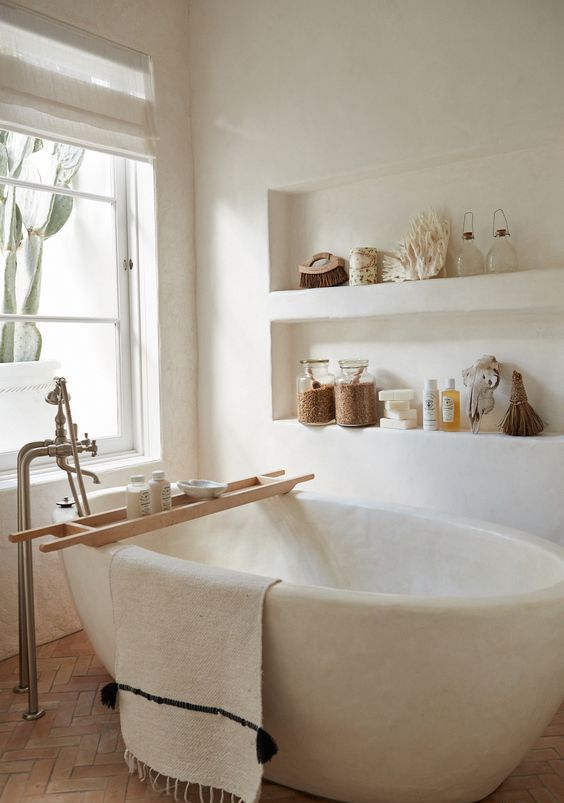 a white bathroom totally clad with plaster, with built-in shelves and with a white stone bathtub