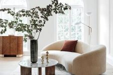 an airy Scandinavian living room with arched windows, a creamy curved sofa, a chic credenza and a three-leg round table, a floor lamp