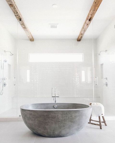 an all-white bathroom with a grey stone bathtub, wooden beams that make the space warmer and catchier