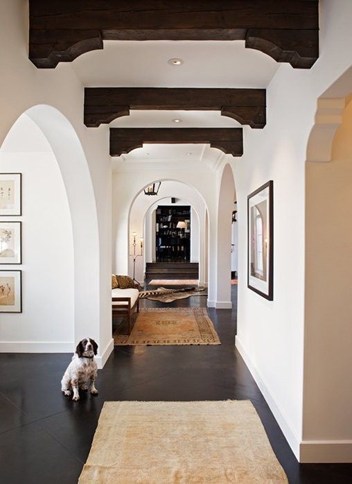 white plaster walls paired with dark floors and dark wooden beams plus arched doorways look very Spanish-like