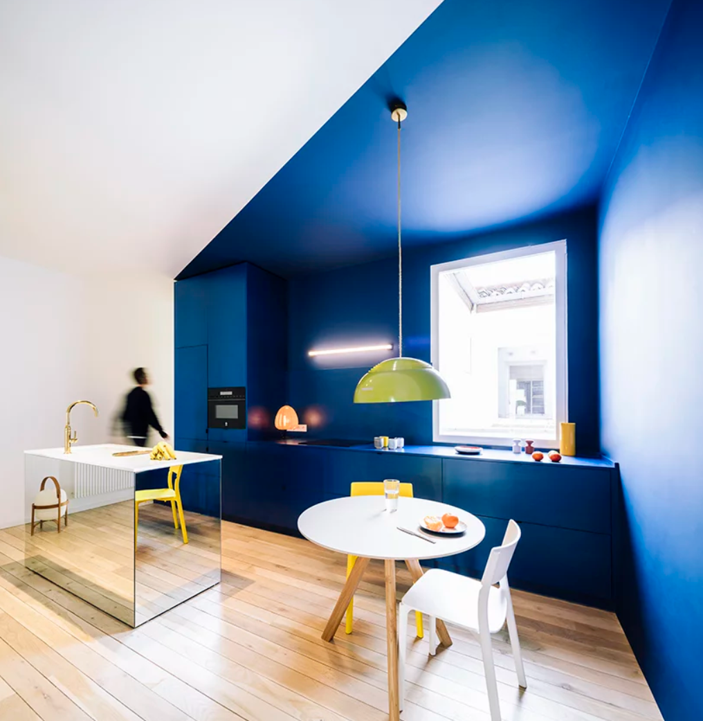The kitchen features bold color blocking, bright blue and white walls, with a mirror kitchen island and a small breakfast space