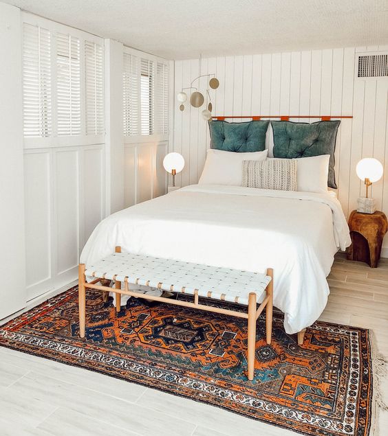 a white boho bedroom with a colorful rug and a blue pillow headboard on a copper holder for a touch of color