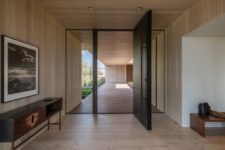 04 The entryway is minimalist, with a dark pivoting door and chic furniture, it’s all done with light-colored wood