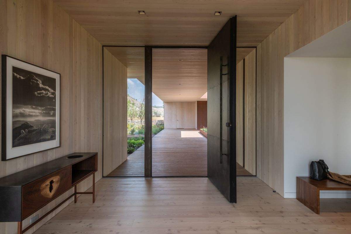 The entryway is minimalist, with a dark pivoting door and chic furniture, it's all done with light colored wood