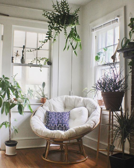 a chic nook with lots of potted plants and a papasan chair of rattan, with a neutral futon and bright pillows