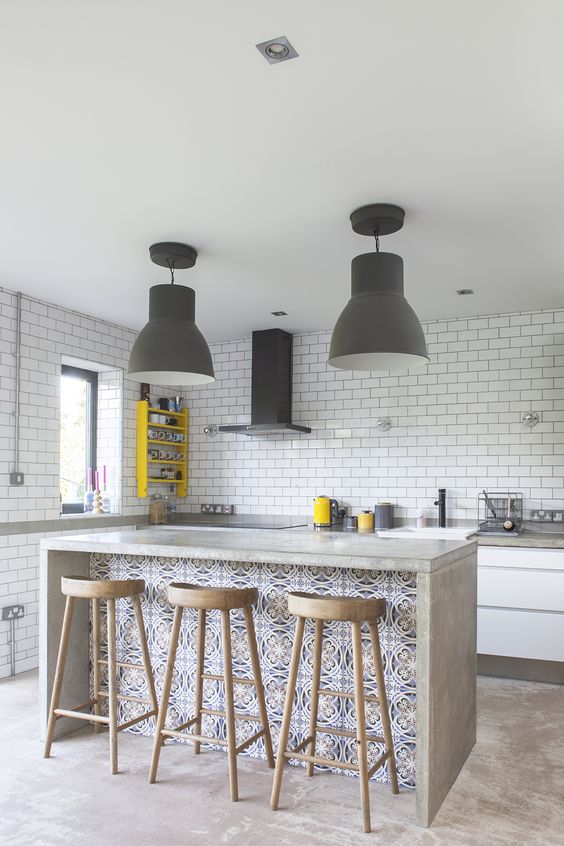 an ultra-modern kitchen done with white subway tiles, a concrete kitchen island with a seating space for dining here