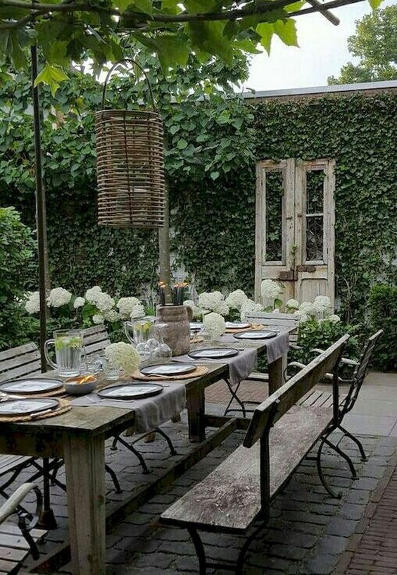 a garden dining space with vintage and shabby chic furniture, wicker lamps and living walls all around