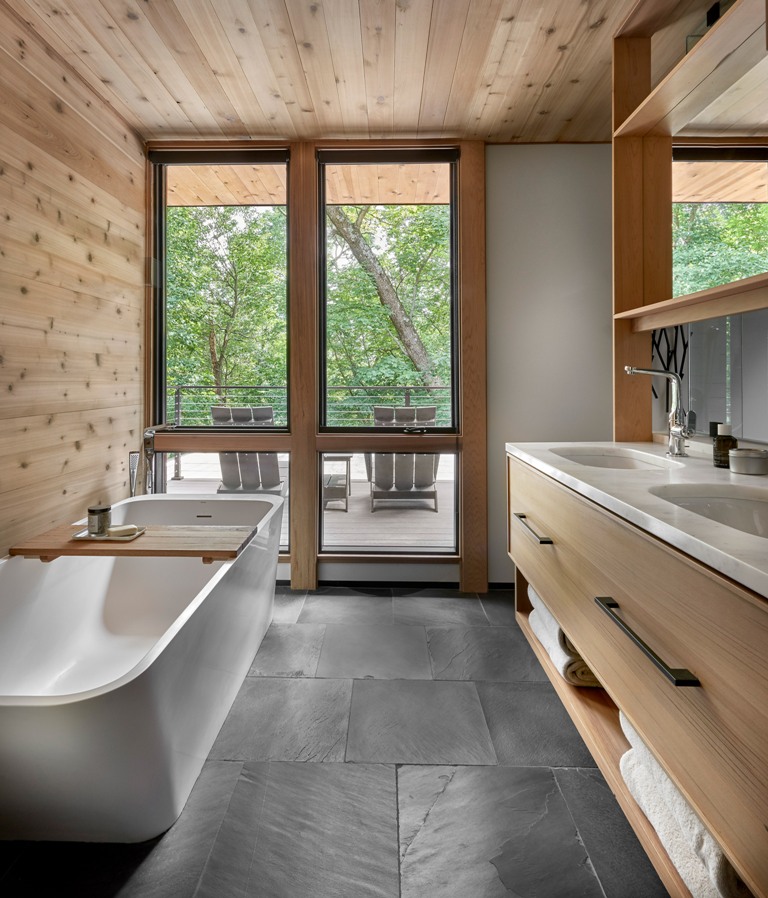 The bathroom is done with dark tiles, lots of wood, a double vanity and a sculptural bathtub