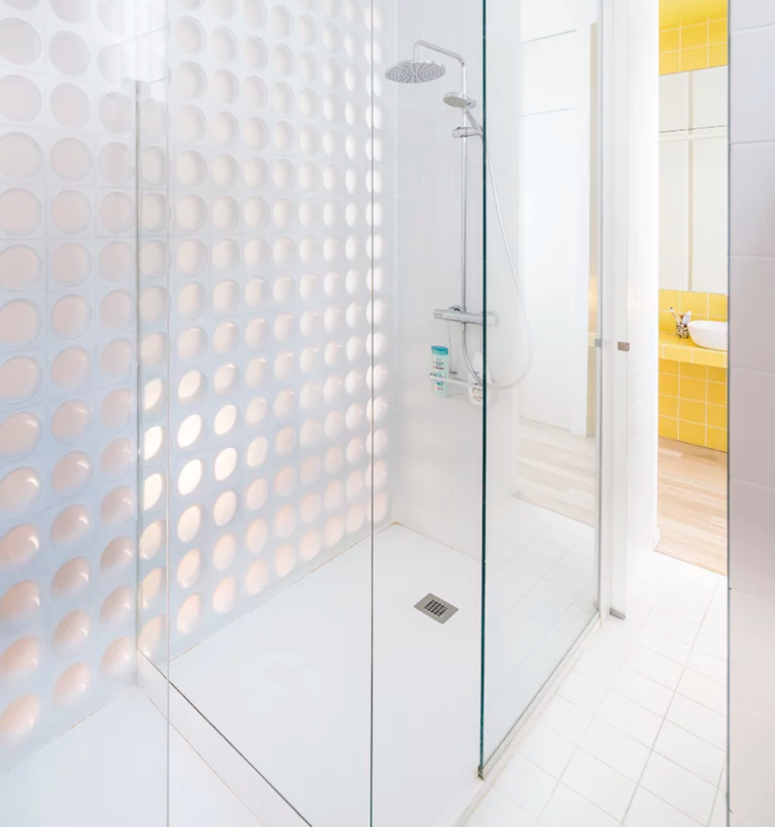 The shower space is all-white, with a perforated wall on one side