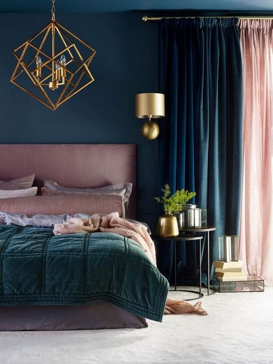 a bold bedroom done in teal, dark green and pink, with a gold planter, a wall sconce and a statement chandelier