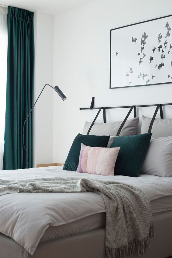 a bright contemporary bedroom done in white, grey and forest green, with grey hanging pillows as a headboard