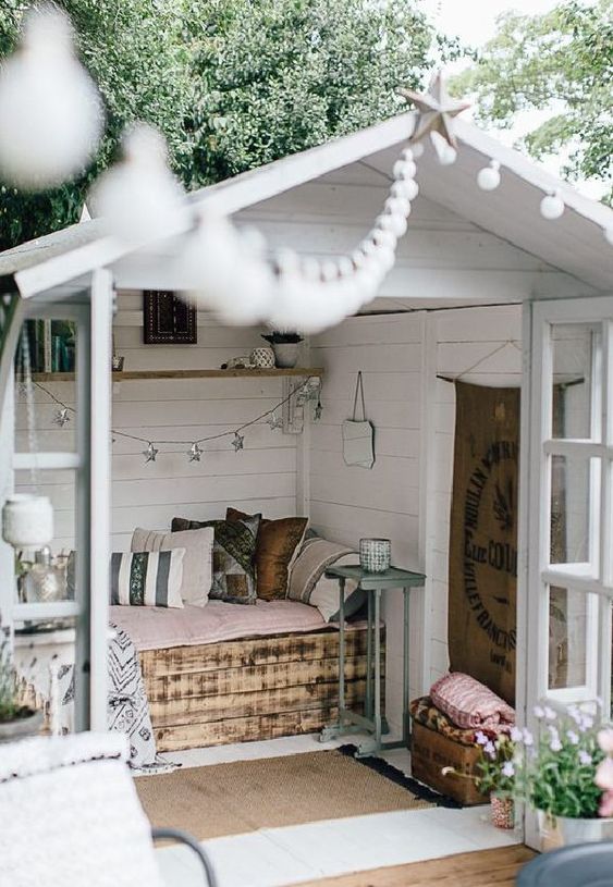 a small garden shed repurposed into a small bedroom with a pallet bed and pastel linens