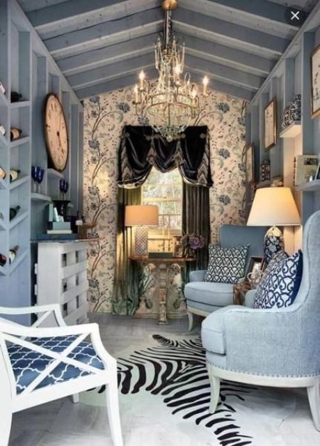 a refined she shed done in blues, with a gorgeous chandelier, a velvet curtain and some elegant accessories