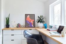 The work space is done with a large corner desk, white cabinets, bold artworks and potted plants