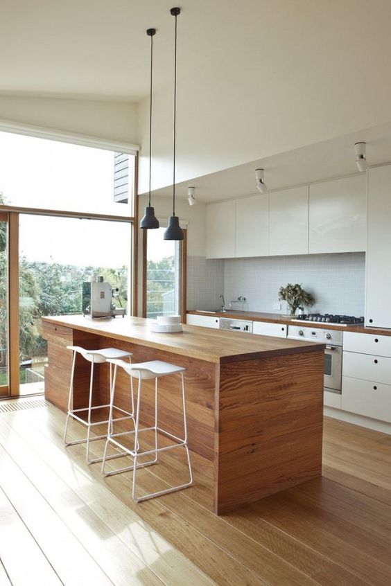 a modern kitchen in white, with a wooden kitchen island that is good both for eating and cooking here