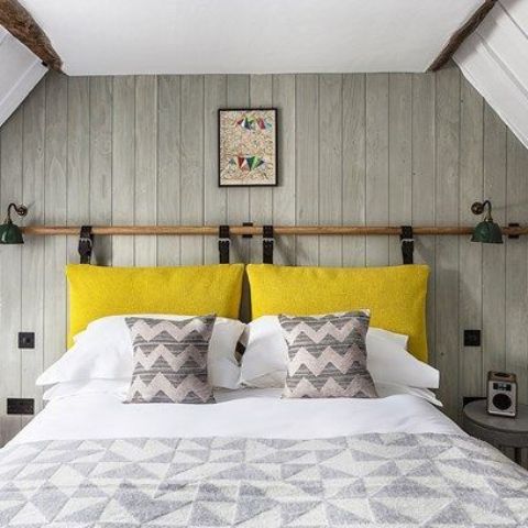 a neutral bedroom with a plenty of pattern and a bright yellow pillow headboard hanging on leather belts looks bright