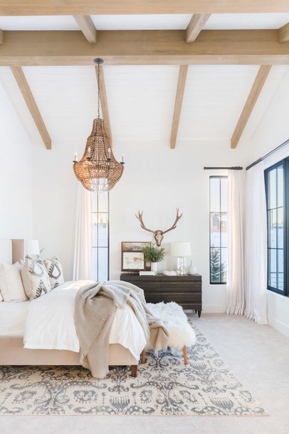 a neutral eclectic bedroom with wooden beams on the ceiling, a statement brass chandelier with candles