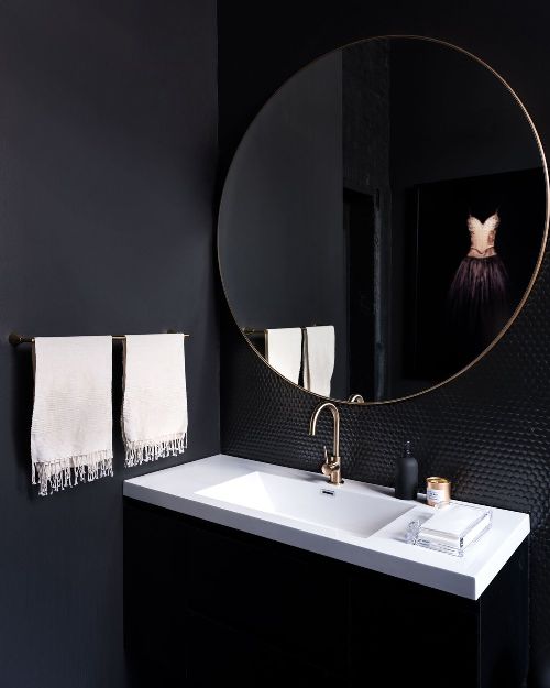 an onyx powder room with a contrasting white sink, white towels and shiny black penny tiles
