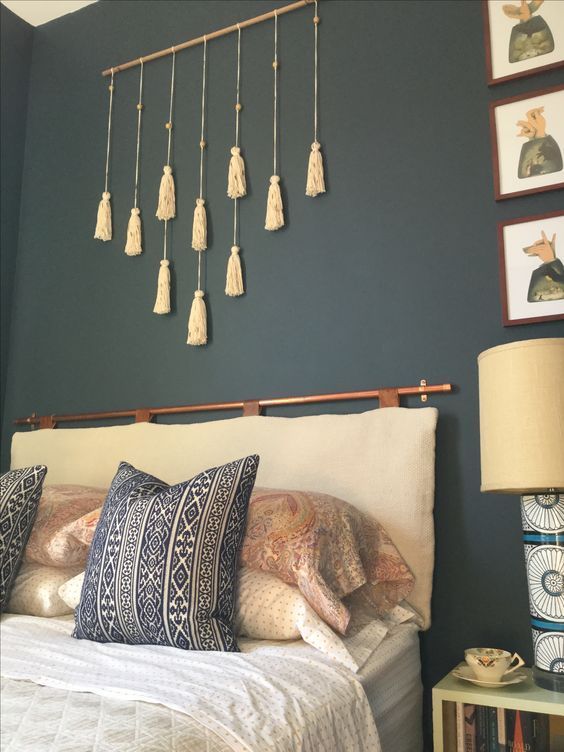 a boho bedroom with a black statement wall, a tassel hanging, a neutral cushion headboard on a copper holder