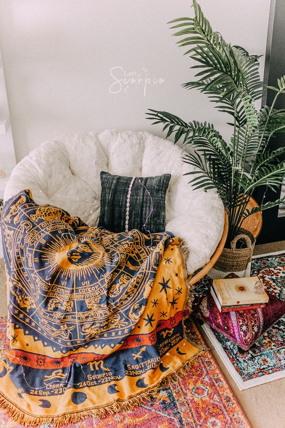 a boho reading nook with a rattan papasan chair with a white futon and a bright zodiac blanket plus a plant and colorful rugs