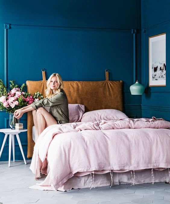 a bright bedroom with bold blue walls, a mint pendant lamp and a bed with a hanging leather headboard