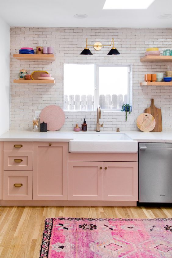 a small kitchen done with pink cabinets, a bright printed rug and neutrals to create a contrast