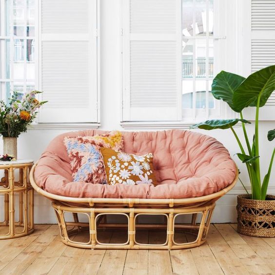 a rattan mamasan chair with a pink futon, floral pillows and blooms and potted plants for a boho space