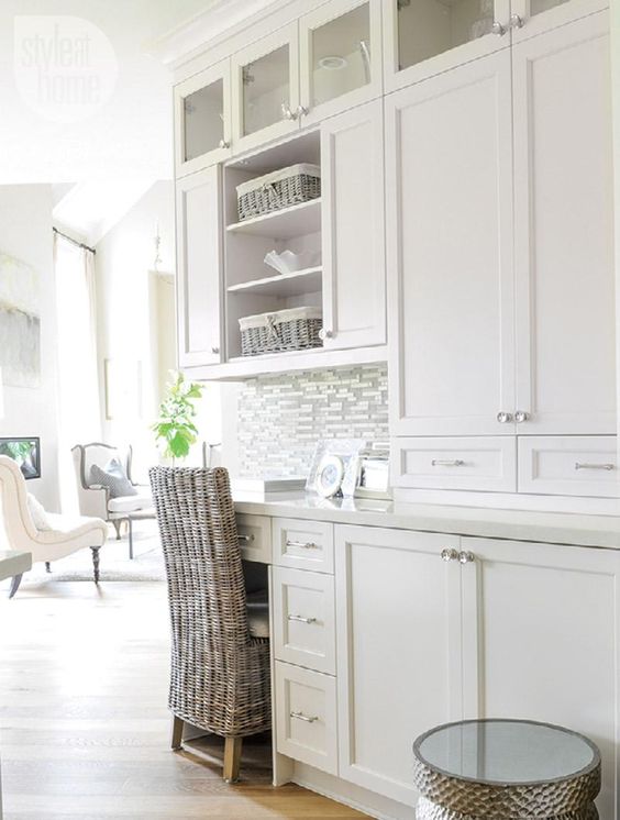 A white rustic kitchen with a built in desk and a woven chair for working or finding out