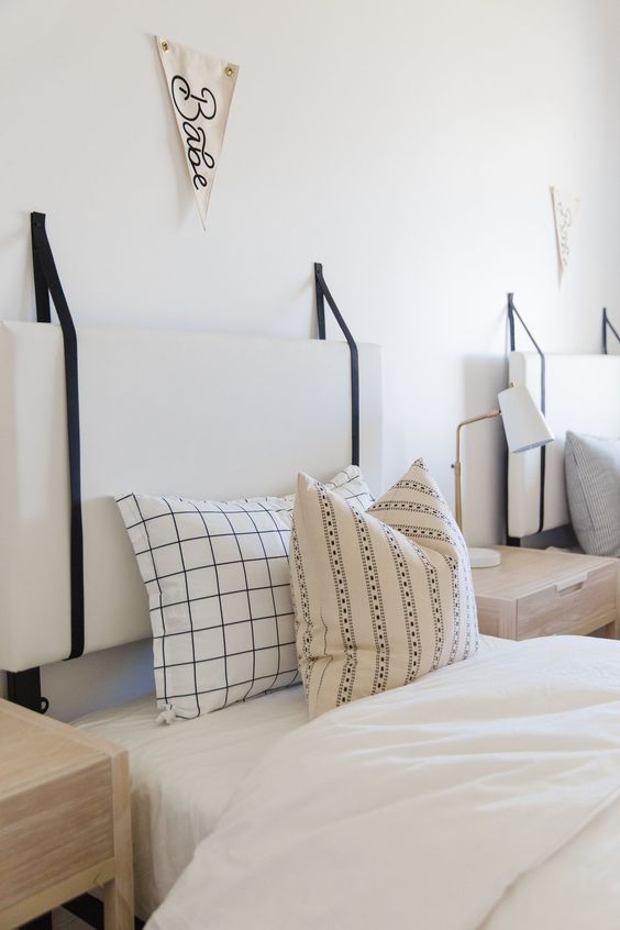 a double guest bedorom with white cushion headboards hanging on black cords looks serene and fresh