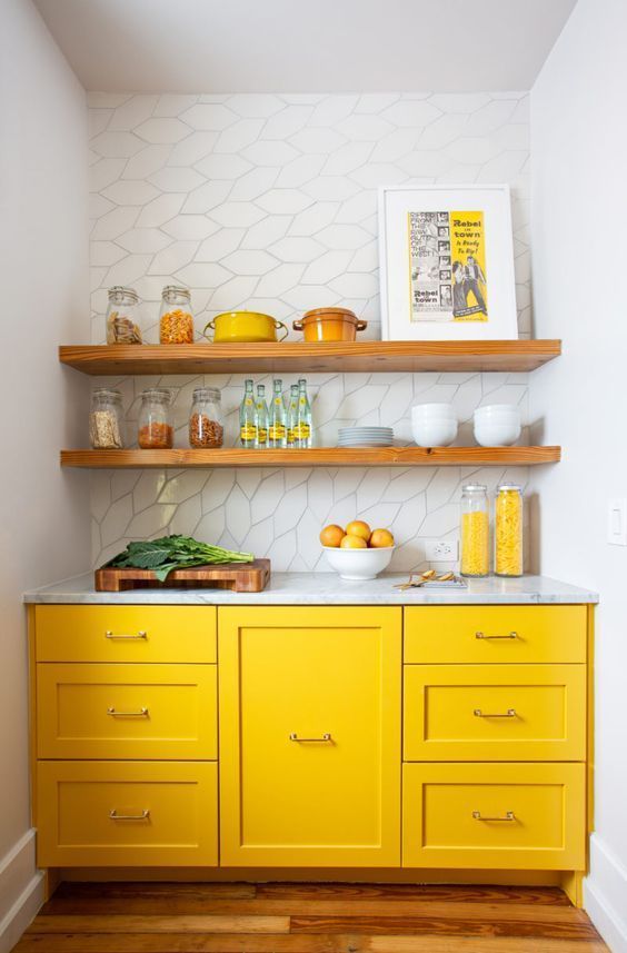 a tiny kitchen with bright yellow cabinets, all whites and wooden shelves over the cabinets