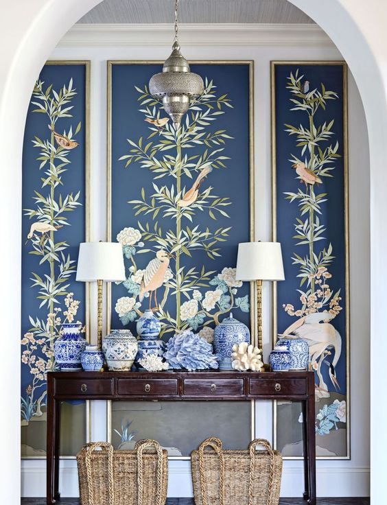 an entryway with a console, blue vases, lamps and dark flora and fauna wallpaper for a statement
