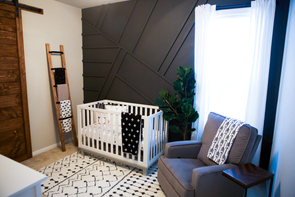 A boho nursery with a black geometric wall and a grey chair to match looks very bold and modern