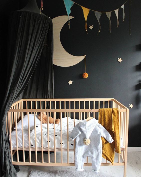 a cute celestial nursery with a black statement wall and a black cnaopy over the crib to make the space peaceful