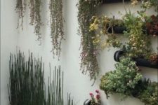 25 a wall with black metal planters with greenery and bright blooms and concrete planters with grasses