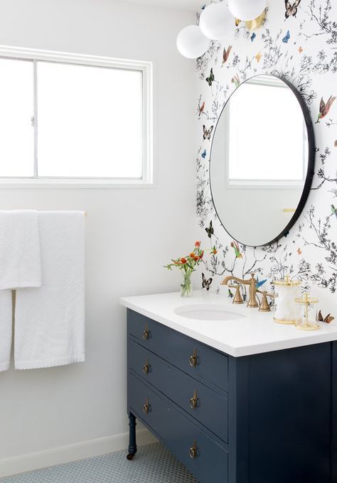a neutral bathroom with a black vanity, floral and fauna wallpaper and a round mirror for a bold look