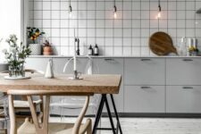 a Nordic kitchen with grey cabinets, a white tile backsplash, sconces that hold bulbs, a table with a cork countertop and wooden chairs