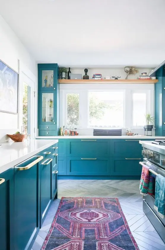 a beautiful blue kitchen with lots of natural light, touches of gold and white countertops plus a backsplash